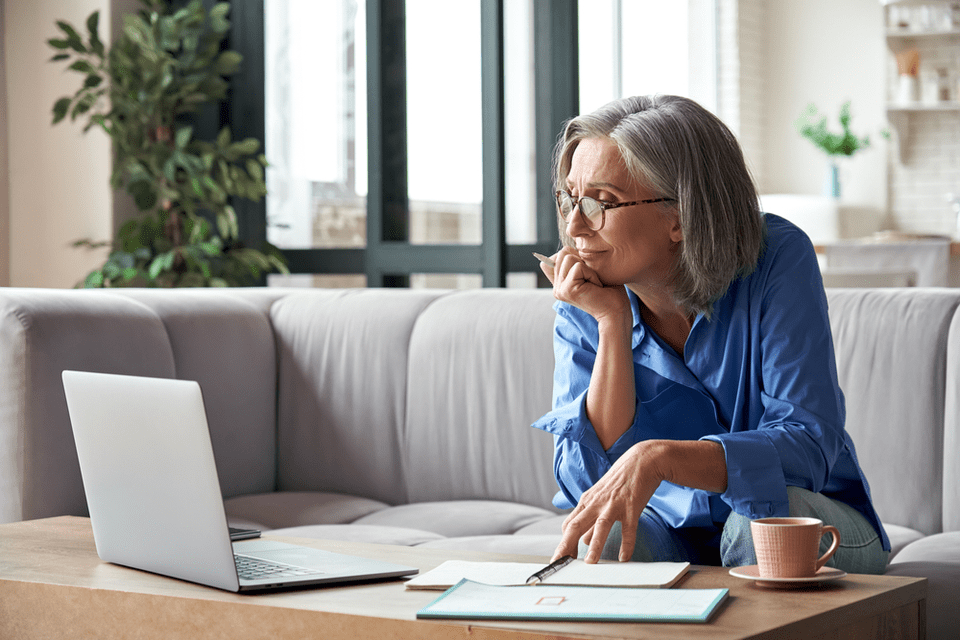 A middle-aged woman sits at the computer in a bright room.